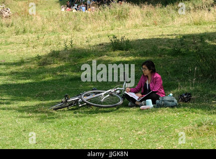 17. Juli 2017 - saß die junge Frau im Schatten eines großen Baumes zeichnen, neben ihrem Fahrrad Stockfoto
