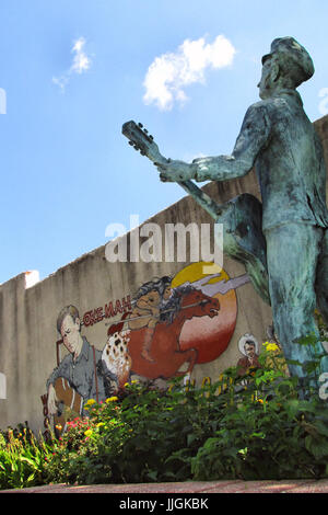 Ein Wandbild und Statue von Woody Guthrie mit seiner Gitarre steht in einem Park in seiner Heimatstadt Okemah, Oklahoma. Stockfoto