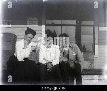 Antike c1910 Foto, drei Erwachsene auf einen Schritt in einem kleinen Laden mit einem Schild für Clicquot Club Ginger Ale an der Wand. Ort unbekannt, möglicherweise Rhode Island, USA. QUELLE: ORIGINALFOTO. Stockfoto