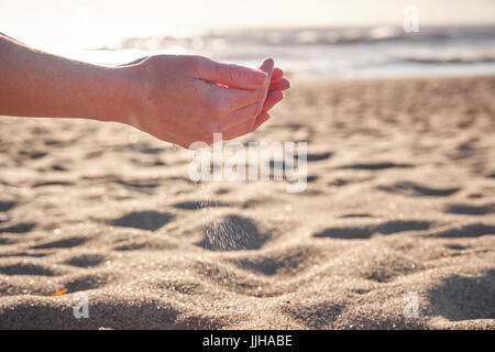 Eine junge Frau, die sieben Sand durch ihre Hände am Strand. Stockfoto