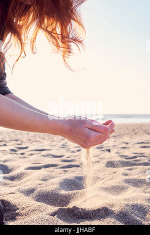 Eine junge Frau, die sieben Sand durch ihre Hände am Strand. Stockfoto