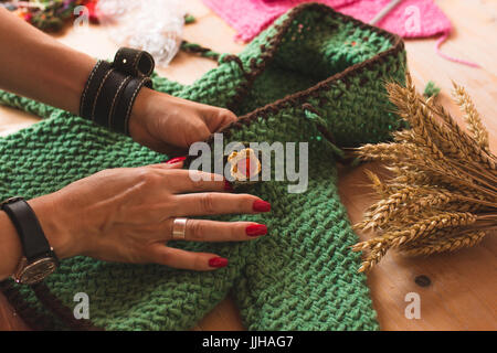 Frau Hand mit rot lackierten Nägeln Qualitätsprüfung handgewebte Babypullover auf einer Holzfläche mit Weizen in der Szene. Stockfoto