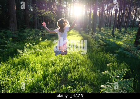 Ein junges Mädchen springen vor Freude in einem sonnendurchfluteten Wald.