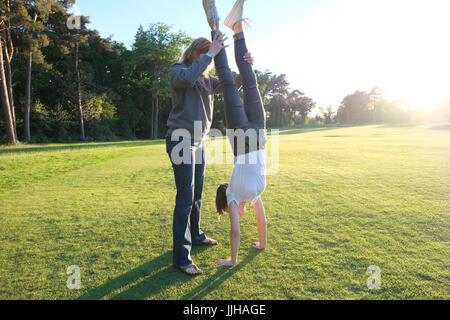 Eine Frau, die helfen, ihre Tochter mit einem Handstand an einem sonnigen Tag. Stockfoto