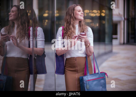 Eine junge Frau überprüft ihr Handy während Sie einkaufen. Stockfoto