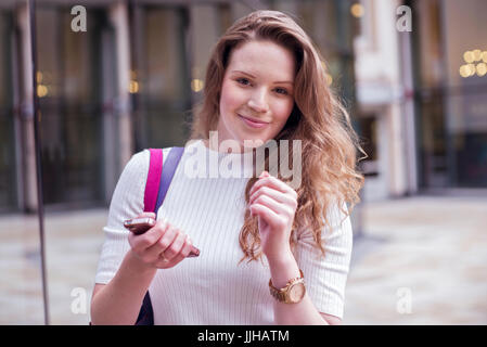 Eine junge Frau überprüft ihr Handy während Sie einkaufen. Stockfoto