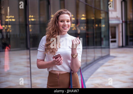Eine junge Frau überprüft ihr Handy während Sie einkaufen. Stockfoto