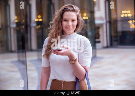 Eine junge Frau überprüft ihr Handy während Sie einkaufen. Stockfoto