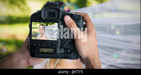 Bild von Händen mit Kamera gegen glückliche schöne Braut mit Seifenblasen beschnitten Stockfoto