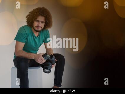 Fotograf mit der Kamera auf den Händen sitzen. Schwarz und gelb Bokeh Hintergrund Stockfoto