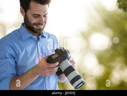 Fotograf sucht die Bilder auf der Kamera. Grün und weiß Leuchten und Fackeln Hintergrund unscharf Stockfoto