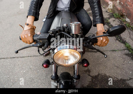 Nahaufnahme von einem Hipster-Biker-Mann hand in Leder Handschuh Halt Gashebel des klassischen Stil Café Racer Motorrad. Fahrrad benutzerdefinierte in Vintage Garage gemacht. Stockfoto