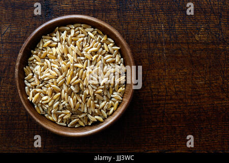 Kamut Weizenkörner in dunklen Holzschale auf dunkelbraunem Holz von oben isoliert. Stockfoto