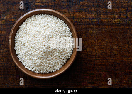 Trockenen Tapioka-Perlen in dunklen Holzschale auf dunkelbraunem Holz von oben isoliert. Stockfoto