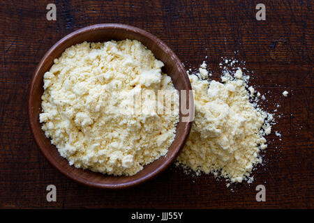 Maismehl in dunklen Holzschale auf dunkelbraunem Holz von oben isoliert. Verschüttete Mehl. Stockfoto