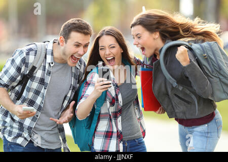 Vorderansicht der drei aufgeregt Studenten erhalten gute Nachricht auf Zeile in einem Mobiltelefon in einem Uni-Campus oder Straße Stockfoto