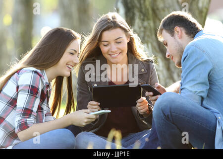 Drei Freunde mit mehreren Geräten im Freien sitzen im Freien in einem park Stockfoto