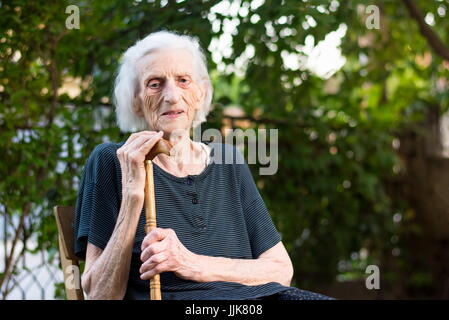 Ältere Frau mit einem Spazierstock im Freien sitzen Stockfoto