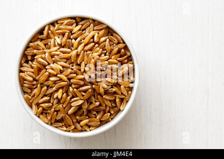 Kamut Weizenkörner in Keramikschale isoliert auf weiß lackiertem weißen Holz von oben. Stockfoto