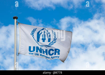Flagge des Hohen Kommissars der Vereinten Nationen für Flüchtlinge (UNHCR) winken in den Wind in der UNHCR-zentrale vor blauem Himmel mit Wolken. Stockfoto