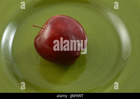 Ende der ganze rohe Red Delicious Apfel auf Teller grün Stockfoto