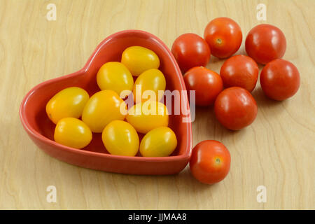 Rote und gelbe Kirschtomaten in und außerhalb von rote Herzförmige Schüssel Stockfoto