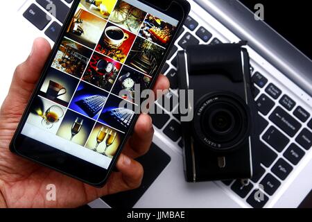 Foto von eine Hand mit einem Smartphone über einen digitalen spiegellose Kamera und Laptop-computer Stockfoto