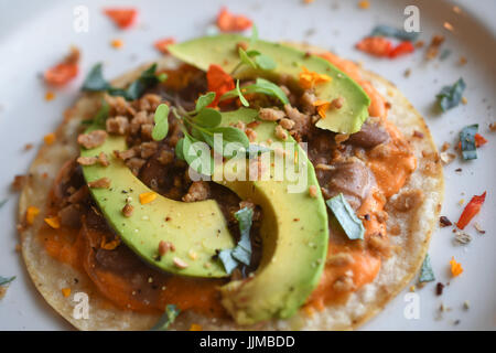 Taco Dienstag, vegane Tacos mit Chorizo-Bohnen, veganen Käse, Avocado, blaue Blume Blütenblatt und eine gelbe Blume. Stockfoto