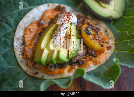 Taco Dienstag, vegane Tacos mit gegrillten Pfirsichen, Vegan Cashew Sahne, Avocado, veganen Käse und Chorizo.  Serviert auf riesigen grünen Blatt auf Null Abfall Veranstaltung Stockfoto