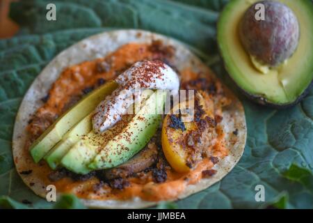 Taco Dienstag, vegane Tacos mit gegrillten Pfirsichen, Vegan Cashew Sahne, Avocado, veganen Käse und Chorizo.  Serviert auf riesigen grünen Blatt auf Null Abfall Veranstaltung Stockfoto