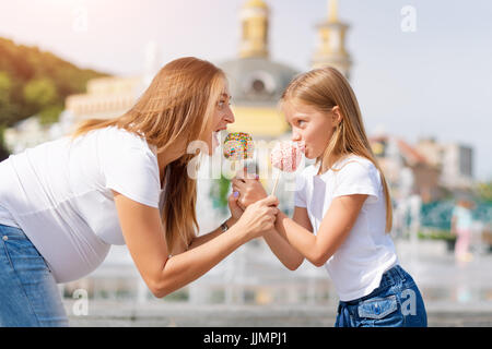 Niedliche kleine Mädchen und ihre schwangere Mutter Essen Liebesäpfel auf Messe im Vergnügungspark. Glücklich liebende Familie. Mutter und Tochter gemeinsam Spaß haben. Stockfoto