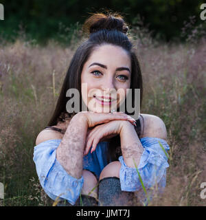 Ein Quadrat von meinem Freund zu beschneiden, als sie auf einer Wiese Wildgras sitzt mit den Knien an ihre Brust und Kinn ruht auf den Händen. Stockfoto