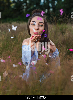 Meine Freundin bläst Elfenbein, rosa und lila farbige Konfetti, geformt in Schmetterlinge, von ihrer Hand, während ein lustiges Sommer-Foto-Shooting in der Nähe von Liverpool. Stockfoto