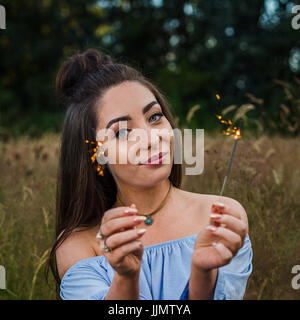 Eine junge Frau spielt mit ein paar Wunderkerzen während ein Porträt zu schießen auf einer Wiese in der Nähe von Liverpool ein Sommer am Abend. Stockfoto