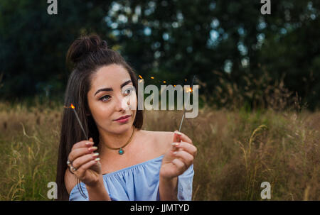 Eine hübsche junge Frau wacht die Funken einer Wunderkerze während einer Outdoor-Portrait-Session auf einer Wiese in der Nähe von Liverpool. Stockfoto