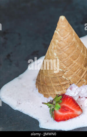 Erdbeereis in einer Waffelhörnchen invertiert und geschmolzen vor einem dunklen Hintergrund, close-up. Stockfoto