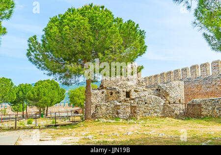 Der Spaziergang durch die Ruinen des alten Schlosses mit der Schale der byzantinischen Kirche hinter den üppigen Pinien, Alanya, Türkei. Stockfoto