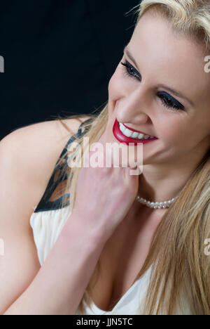 Schöne blonde Frau trägt roten Lippenstift suchen entfernt lächelnd Hand Hals berühren Stockfoto