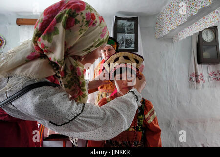 Die russische Frau in traditioneller Tracht legt den Kokoschnik-Brautkopf, um den Sarafan auf den Kopf einer Braut während einer traditionellen Hochzeitszeremonie zu begleiten.Reenactment im Dorf Sibirjachiha, das seine Mitglieder die Bräuche der Altgläubigen mit Stiftungen aus Hunderten von Jahren im Bezirk Soloneshenskiy in der Altai-Region bewahren Eine Region in Westsibirien, Russland Stockfoto