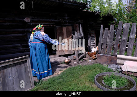 Eine ältere Russin, die traditionelles Sarafan-Kleid trägt und Hühner im Dorf Sibirjachiha füttert, dessen Mitglieder die Bräuche und Traditionen der Altgläubigen bewahren, mit hunderten von Jahren zurückreichenden Fundamenten im Bezirk Soloneshenskiy der Region Altai in Westsibirien, Russland. Die Alten Gläubigen oder Alten Ritualisten sind östliche orthodoxe Christen, die die liturgischen und rituellen Praktiken der russischen Kirche beibehalten, wie sie vor den Reformen des Patriarchen Nikon von Moskau zwischen 1652 und 1666 waren. Stockfoto