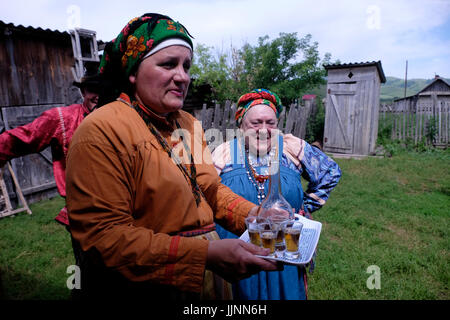 Russische Frauen in traditionellem Sarafan-Kleid servieren hausgemachtes, destilliertes alkoholisches Getränk aus Samogon im Dorf Sibirjachiha, dessen Mitglieder die Bräuche der alten Gläubigen bewahren und deren Fundamente Hunderte von Jahren im Soloneshenskiy-Viertel in Altai Krai, einer Region in Westsibirien, Russland, zurückreichen Stockfoto