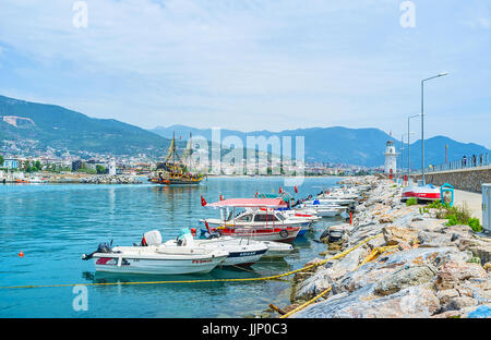 ALANYA, Türkei - 9. Mai 2017: Die Reihe der kleine Holzboote, entlang der Pier mit dem weißen Leuchtturm im Hintergrund, am 9. Mai in Alanya festgemacht. Stockfoto