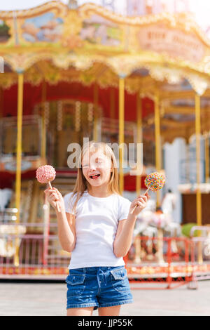 Niedliche kleine Mädchen essen Liebesapfel und posiert auf Messe im Vergnügungspark. Stockfoto