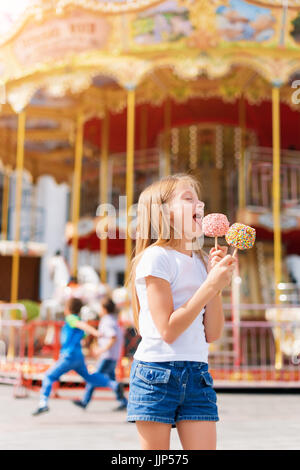 Niedliche kleine Mädchen essen Liebesapfel und posiert auf Messe im Vergnügungspark. Stockfoto
