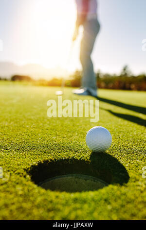 Golfball am Rand des Loches mit Player im Hintergrund. Profi-Golfer setzen Kugel in das Loch an einem sonnigen Tag. Stockfoto