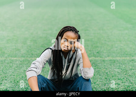 Die verärgert afro-amerikanischen Teenager ist sitzen auf dem Rasen und stützte sich auf ihre Hand. Stockfoto