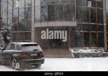 Schneefall in der Stadt vor Weihnachten. Ein einsames Auto steht vor dem Gebäude. Stockfoto