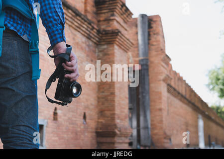 junge asiatische Mann trug blaues Hemd und Jeans mit Kamera und Rucksack Stand in der Nähe alte orange Mauer Stockfoto