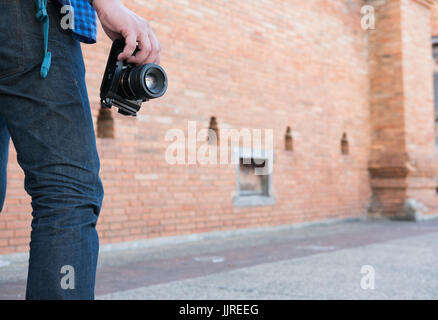 junge asiatische Mann trug blaues Hemd und Jeans mit Kamera und Rucksack Stand in der Nähe alte orange Mauer Stockfoto