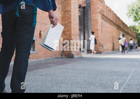 junge asiatische Mann trug blaues Hemd und Jeans mit Karte und Rucksack Stand in der Nähe alte orange Mauer Stockfoto